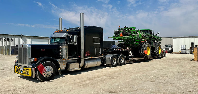 Blue semi carrying a large piece of green farm equipment. 