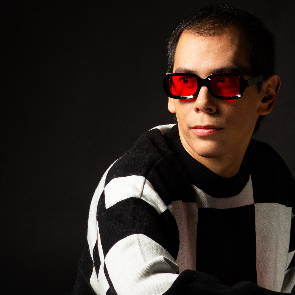 Sexy modelo masculino que viste un suéter blanco y negro Sentado en una silla vintage de plástico rojo transparente vistiendo