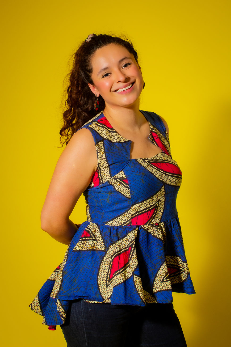 Hermosa joven de cabello largo rizado vestida con un colorido vestido corto en rojo y azul está siendo retratada con una cáma