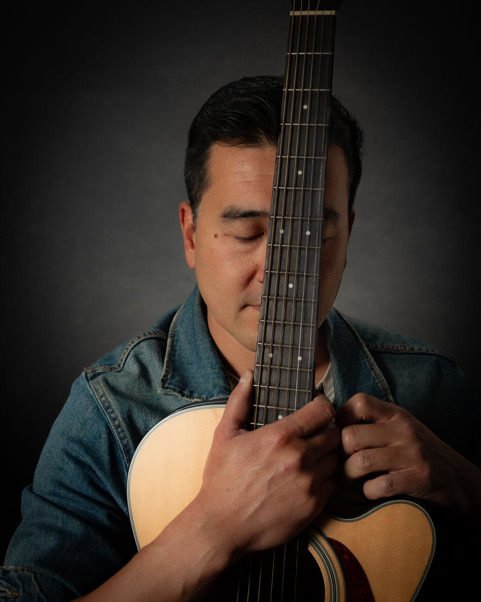 Guitarrista profesional de origen asiático está posando para esta fotografía profesional realizada en el estudio Roma 1 en la