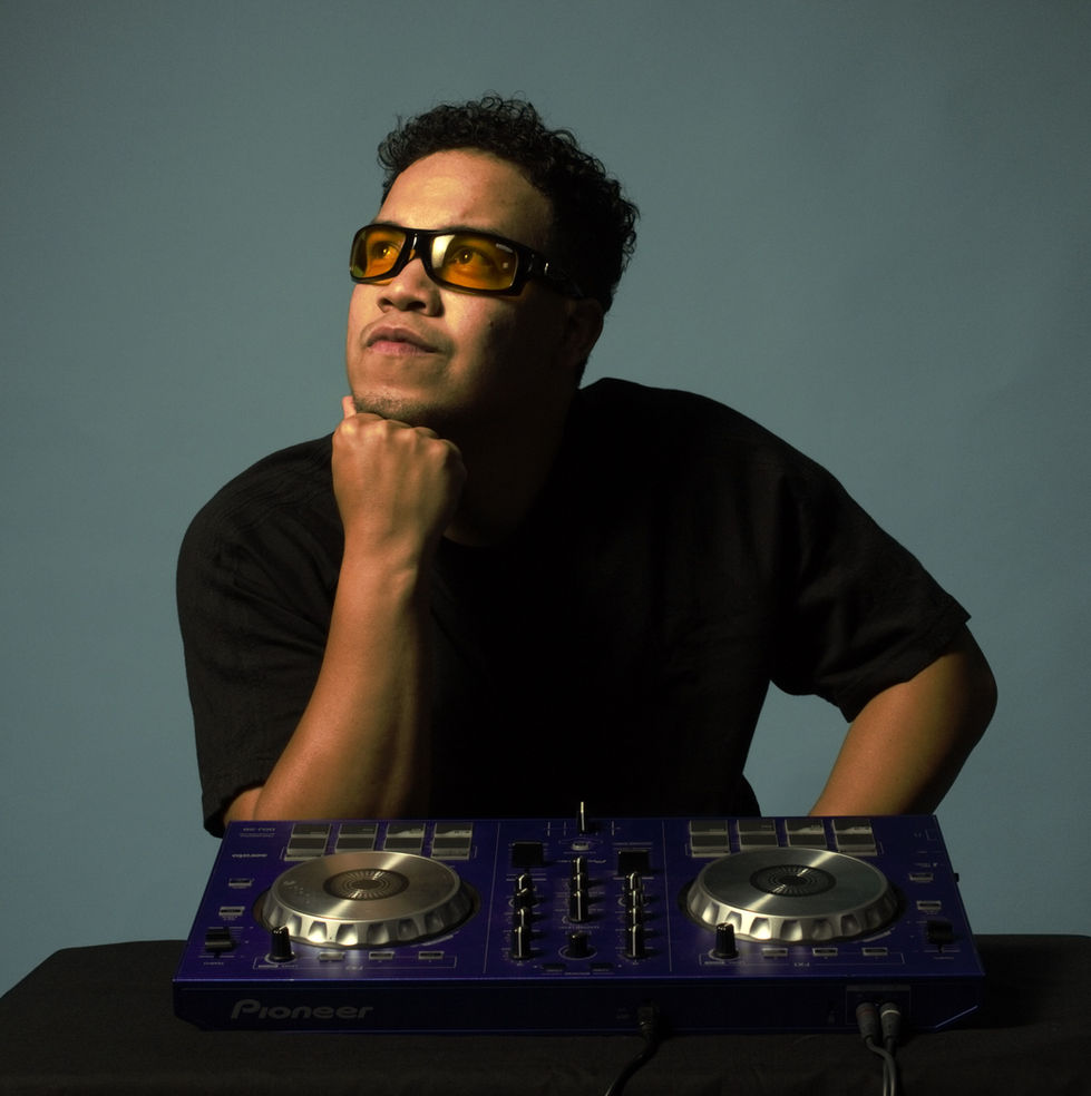 Joven de cabello corto y rizado estilo latino posando como Dj junto con su controlador para realizar esta fotografía profesio