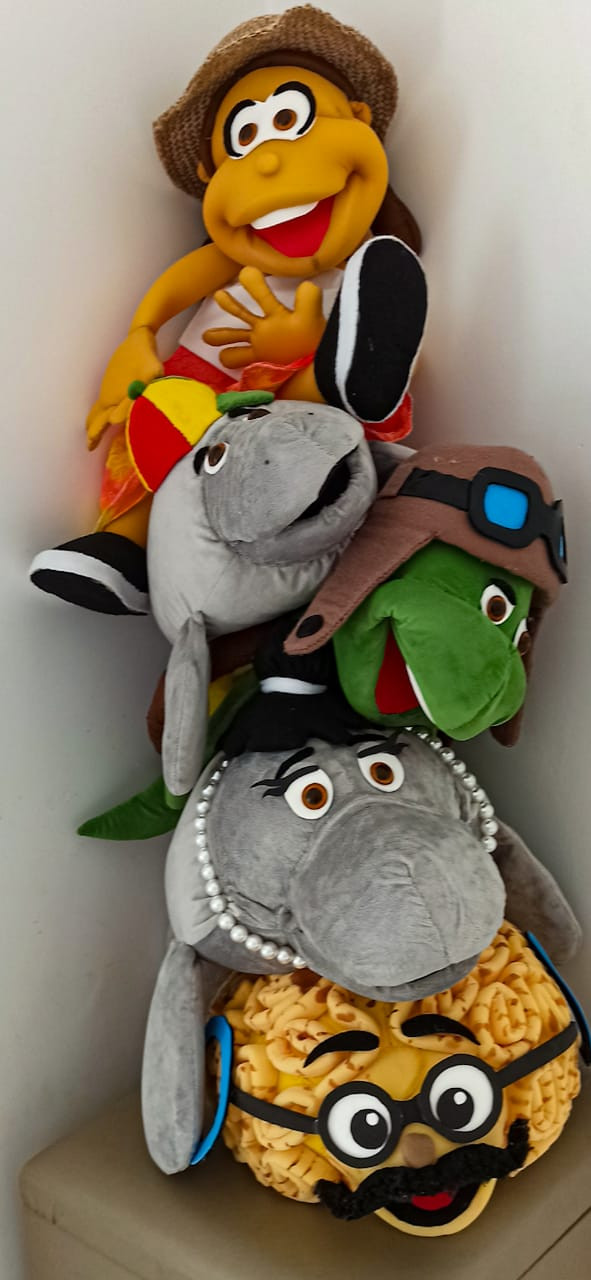 Fantoches dos personagens da série Mar a Vista. Observamos um coral cérebro amarelo com bigode e óculos que na série faz papel de professor. Depois vemos uma peixe boi fêmea cinza com colar de pérolas que é mãe de Tutu, um peixe boi criança que é o personagem principal da série. Tutu veste um chapéu vermelho e amarelo. Também observamos uma Tartatuga de chapéu e óculos e um humano com chapéu de palha de pescador.