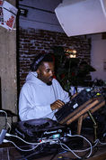 A black man wearing a grey hoodie with a headset on who is djing.