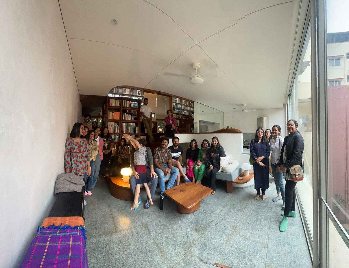 People gathered in a modern, light-filled living room with large windows, off-grid, sustainable architecture, Bangalore.