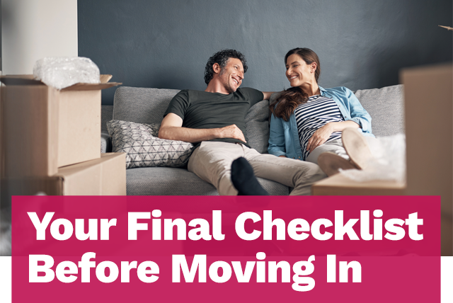 A smiling couple sitting on a couch with moving boxes surrounding them