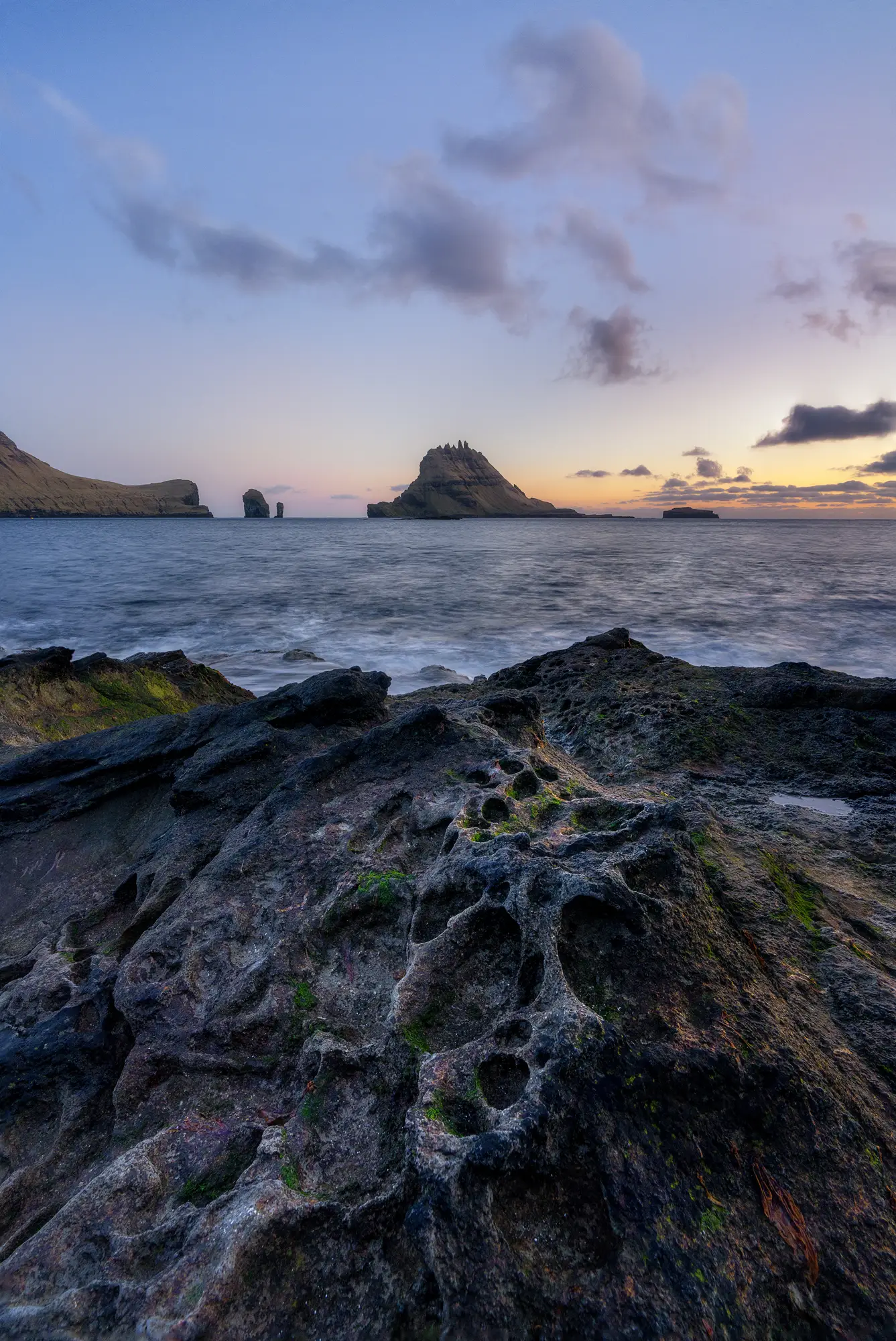 Raue, vulkanische Felsformationen an der Küste der Färöer-Inseln im Abendlicht. Das Meer und die fernen Inseln bilden eine dramatische Kulisse für Landschaftsfotografie