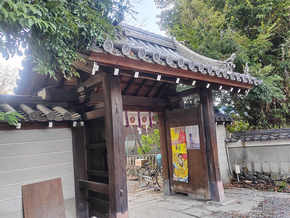 Weathered wooden entrance gate with traditional grey clay roof tiles leading into the shrine grounds.