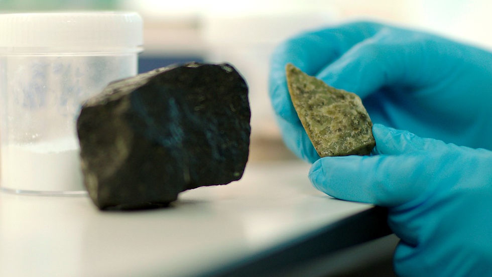 Gloved hand holding a small piece of green olivine rock next to a container of white powder