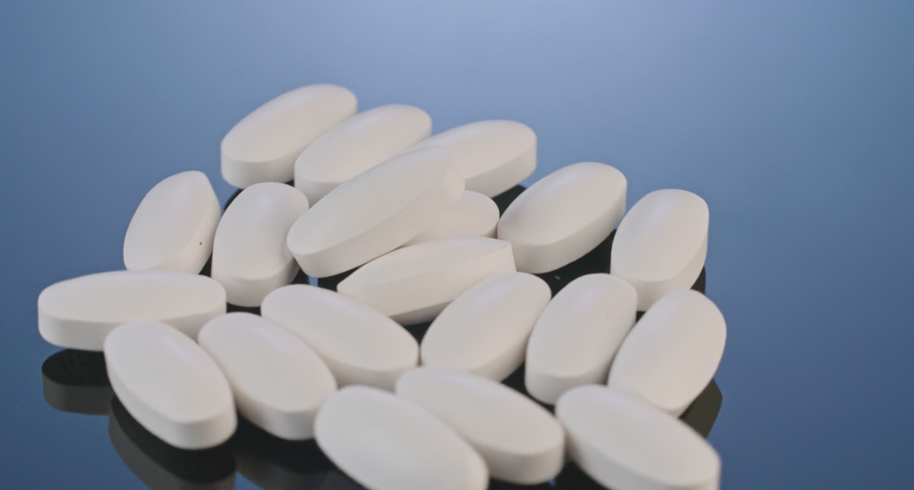Close up of white oblong dietary supplement pills on a clean reflective surface