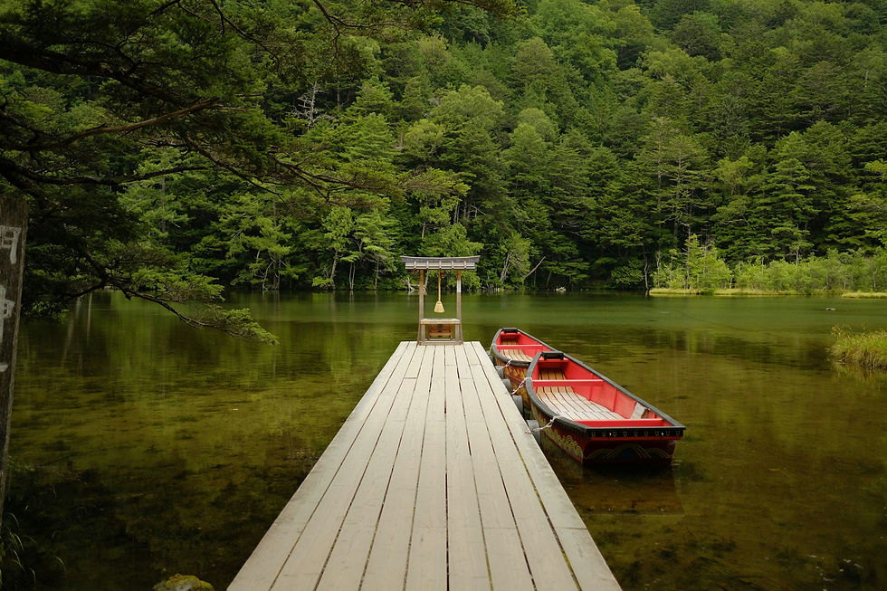 Wooden dock on a calm green lake with two red boats, surrounded by dense forested hills and a serene, secluded mood. Nagano, Japan summer vacation traveling Japan.