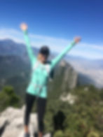 Cristy Mesta en la cima de la M de Chipinque, en Monterrey, con los brazos en alto y una vista panorámica de montañas al fondo.