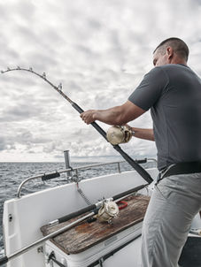 Man fishing with rod on boat, waves, Salty Anchor Charter