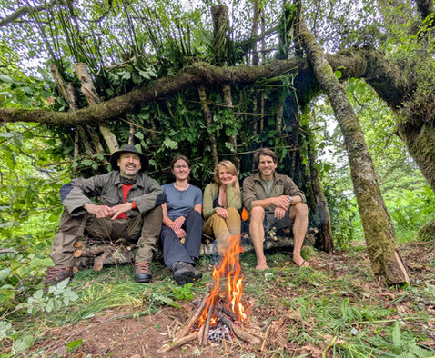 a group making a bushcraft shelter on a bushcraft course and sitting in the shelter with a fire