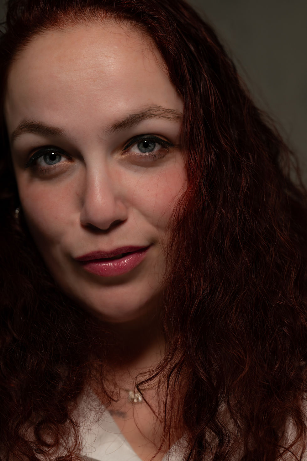 Vrouw met roodachtig krullend haar en blauwe ogen kijkt glimlachend.