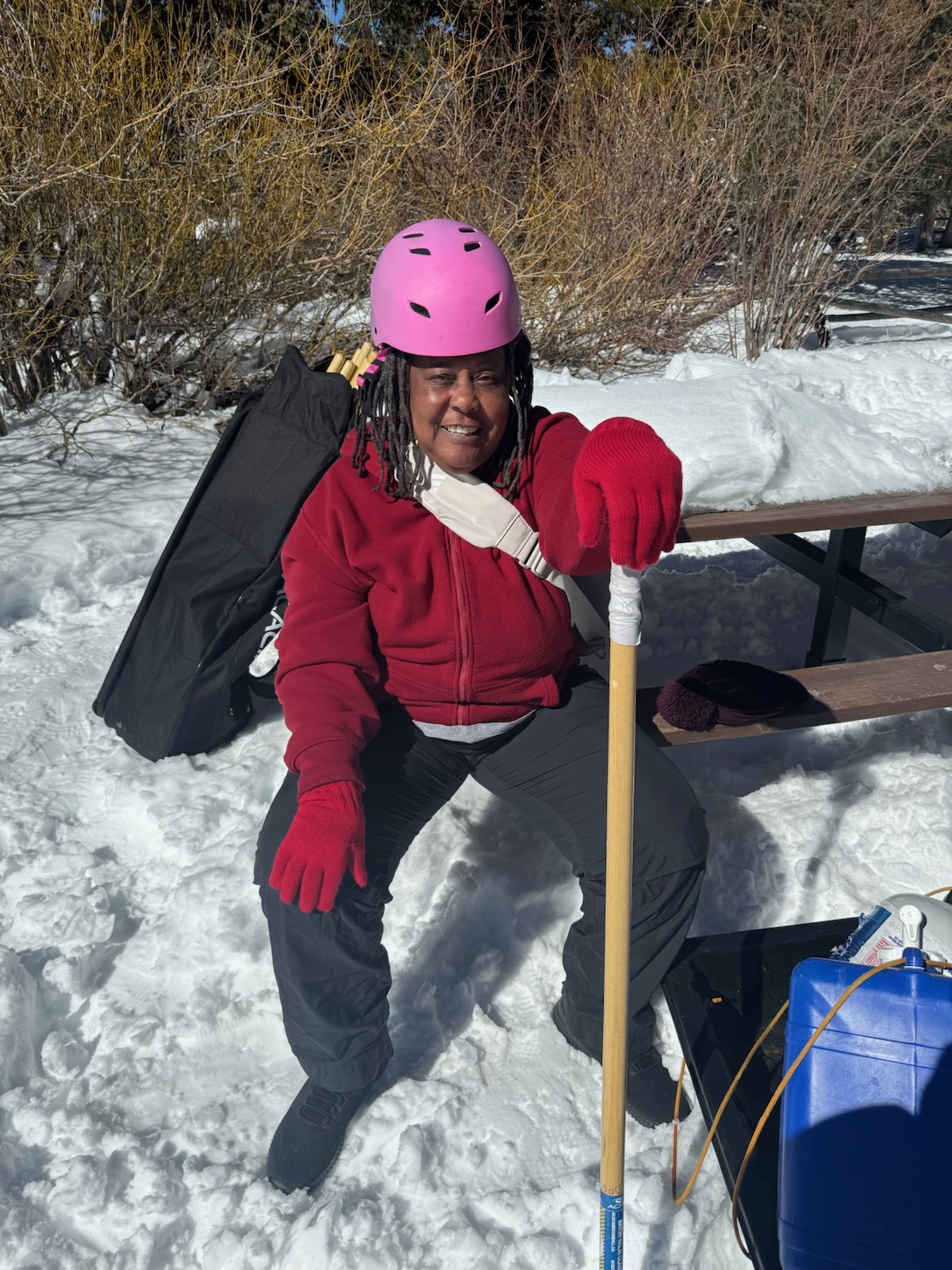 Ms. Sandy's black hair is framed by a pink helmet. Behind her, there is snow.