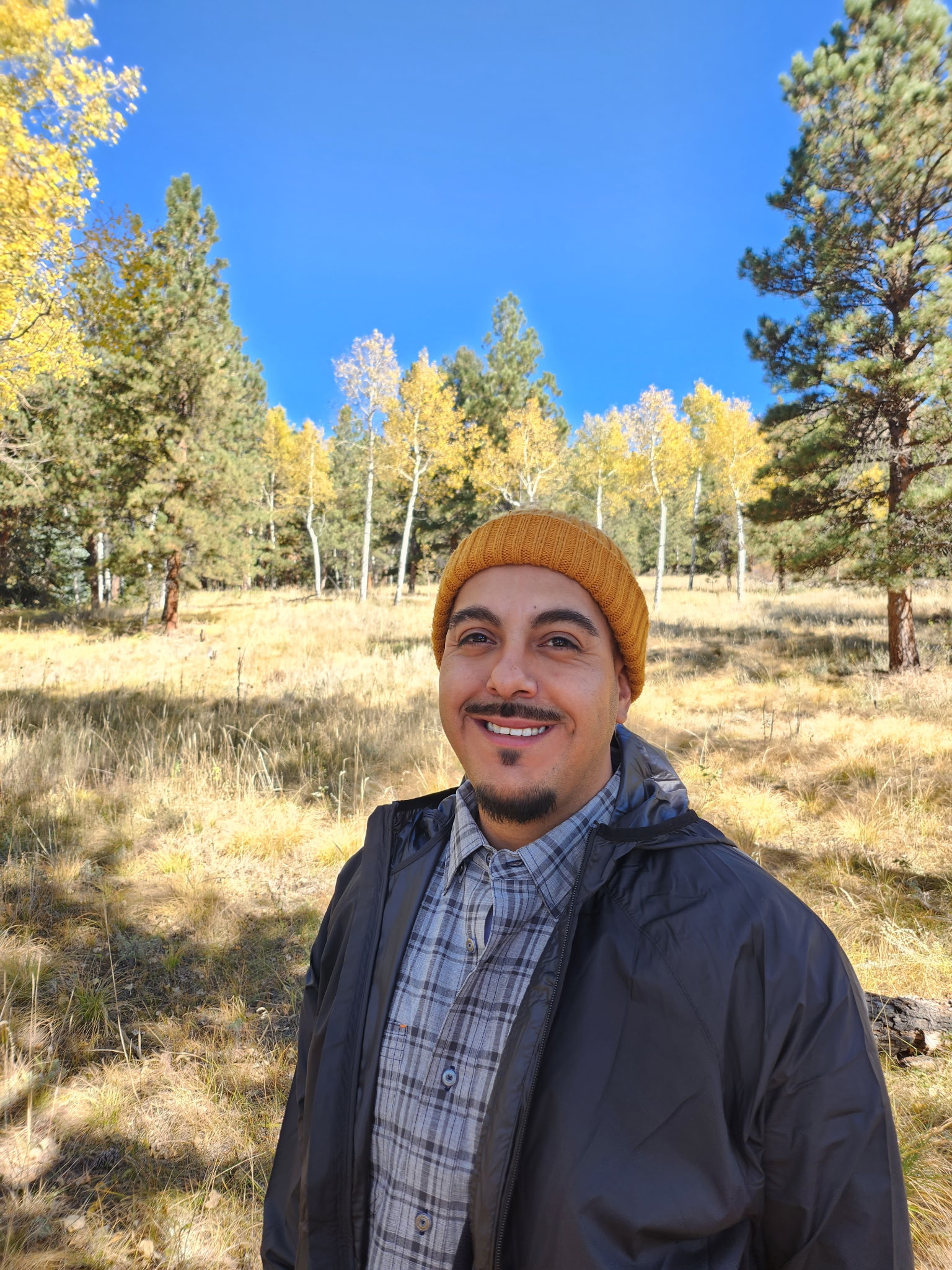 Manny has a brown mustache and goatee — he's smiling and wears a yellow stocking cap.