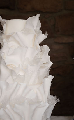 Sculptural white wedding cake with organic ruffles against a raw Highland stone wall in Scotland.