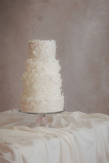 Four-tier all-white sculptural wedding cake by Copper Rose, featuring hand-torn fondant ruffles and luminous, fine art textures, Scotland.