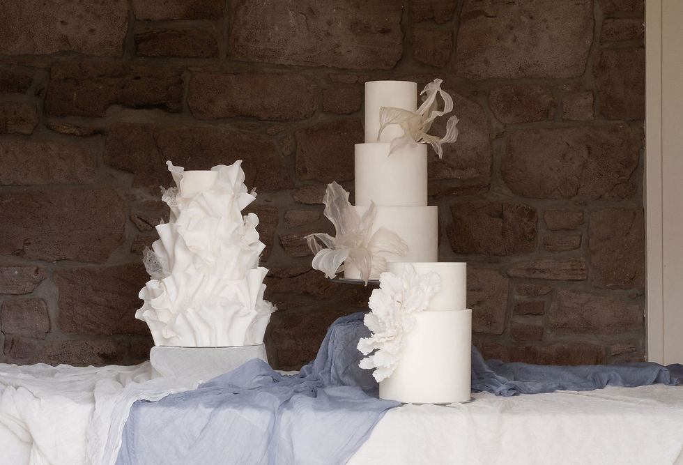 three bespoke wedding cakes set up on display at a wedding venue in scotland, artistic style with soft draping, in front of a natural stone wall