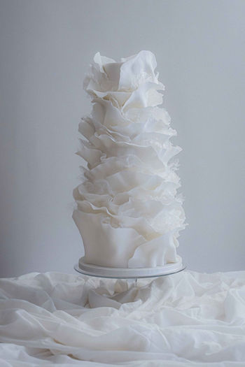 Tall white sculptural wedding cake with meticulous hand-torn ruffles by Copper Rose, displayed at Dunkeld House Hotel, Perthshire, Scotland.