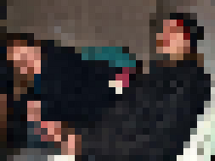 Two people sitting on white chairs indoors, possibly in relaxed or sleepy postures. The background is plain, and lighting is dim.