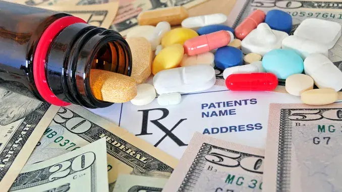 An overturned amber pill bottle spilling colorful tablets and capsules onto a prescription form and fanned US dollar bills.
