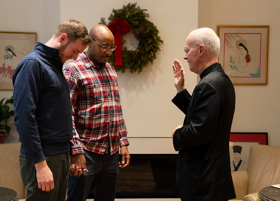 Two men holding hands heads down priest blessing them