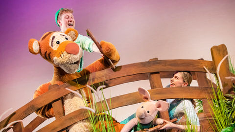 Tigger and Piglet drop sticks into a stream from a bridge.