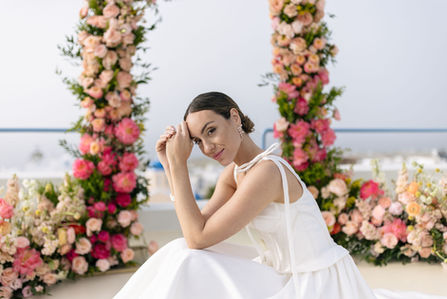bride in dress with bow on shoulder poses in front of a lush floral arch