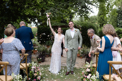 bride and groom walk down the aisle in a shower of rose petals as the bride raises her bouquet