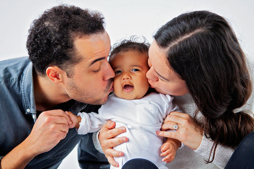 father and mother kissing cheeks of baby face