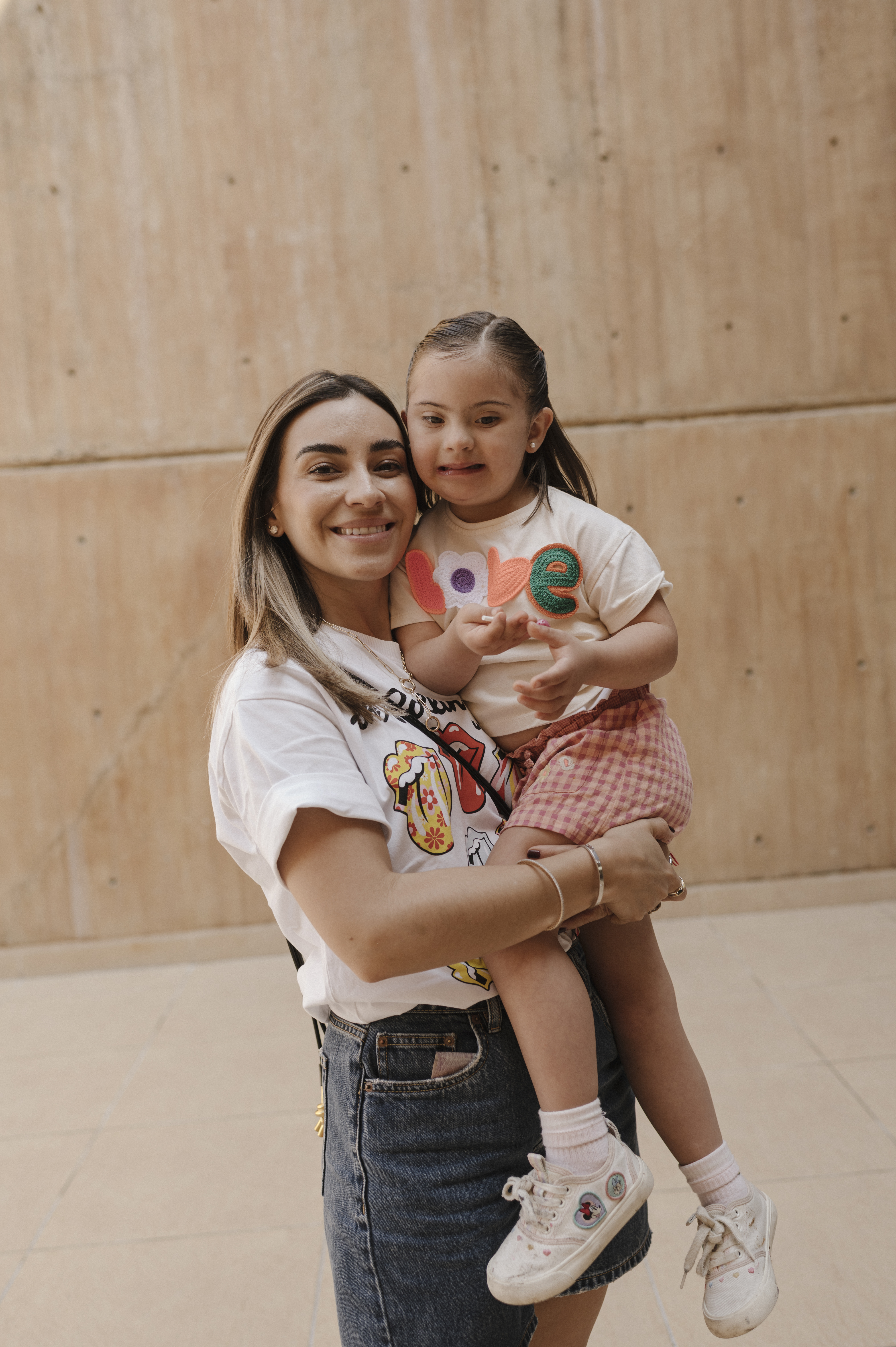 Mujer joven sonriendo mientras sostiene a una niña pequeña con síndrome de Down