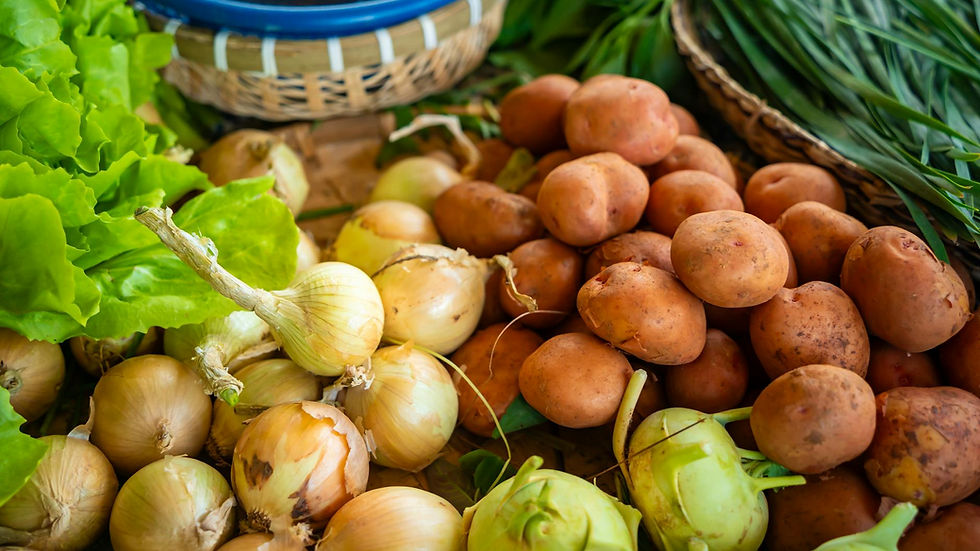 Close-up of assorted fresh vegetables including onions, potatoes, and greens at a farmers market stall.