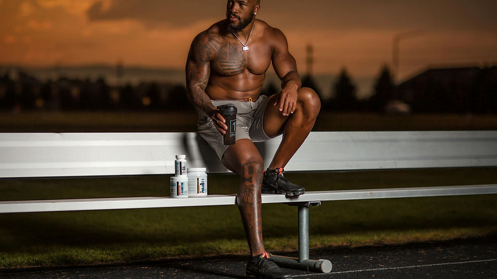 Muscular athlete sitting on a bench with supplements, enjoying a sunset at an outdoor stadium.