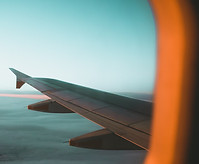 Vue aérienne depuis le hublot d’un avion, montrant une aile d’avion au-dessus d’un ciel clair teinté de bleu et d’orange