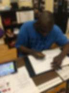 Adult student writing in a binder with speech device on the table