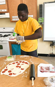 Adult student wearing rubber gloves making a pepperoni pizza