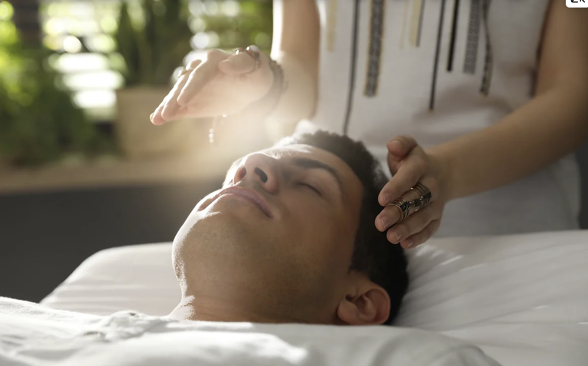 Image of a person's feet as they lie down, receiving Reiki. A Reiki practitioner is holding their hands a small distance above the soles of their feet providing energy healing
