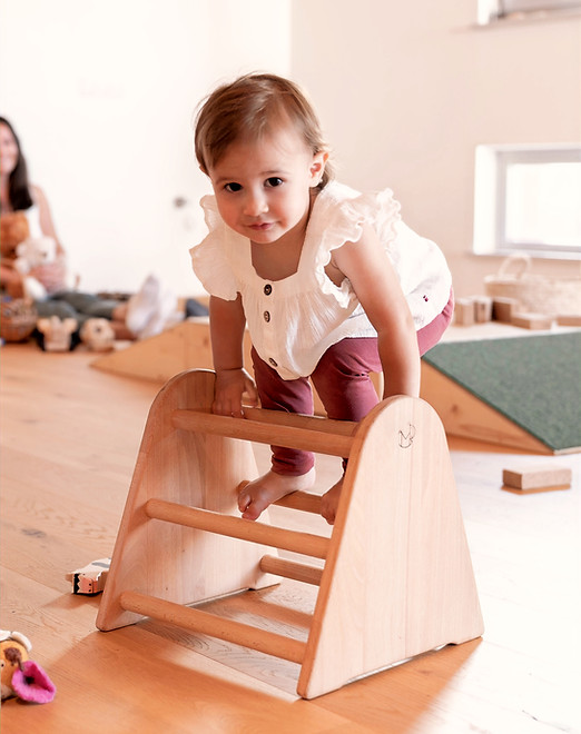Mädchen klettert über ein kleines Holz-Gerüst in einem Emmi Pikler Spielraum