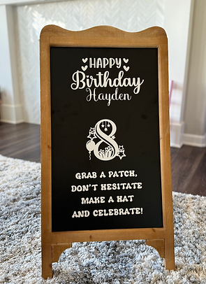 Custom birthday party welcome sign on wooden chalkboard easel featuring patch party instructions — 'Grab a patch, don’t hesitate, make a hat and celebrate!' — designed for Hayden’s 8th birthday hat decorating party by Katie’s Party Lab in Erie, Colorado.