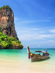 Bateau traditionnel à Phuket sur des eaux cristallines, avec des falaises et un ciel bleu.