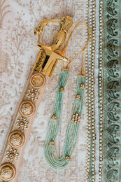 Detail of the groom's kirpan and green bead necklace on embroidered fabric before a Sikh wedding at Hard Rock Los Cabos
