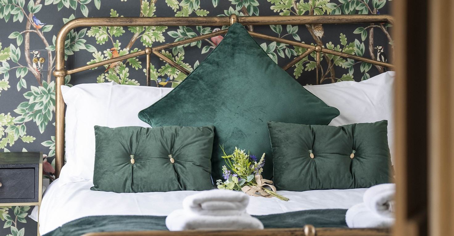 Bed with deluxe green cushions and patterned wall paper
