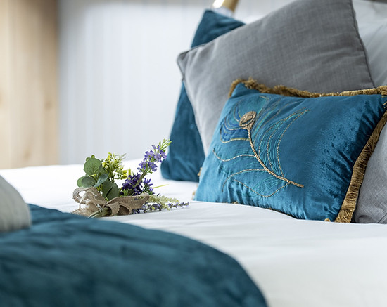 beautifully set bed with teal cushions and fleece cover and white linen