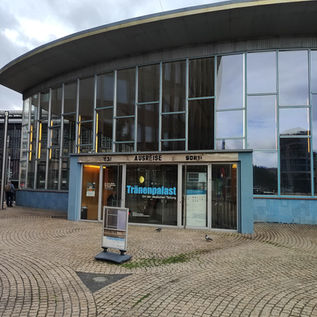 Вход в музей Трэненпаласт в Берлине, с изогнутым фасадом в стиле модерн с большими стеклянными окнами и вывеской музея.