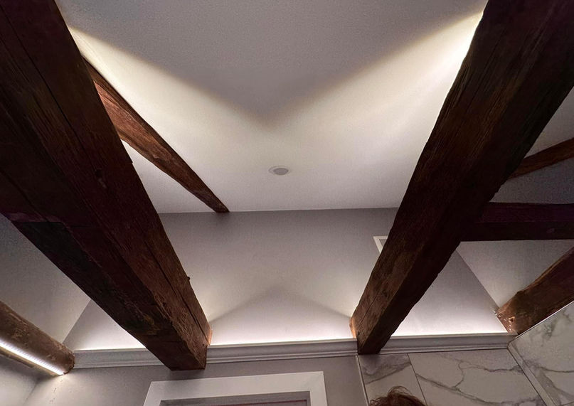 Architectural indirect LED cove lighting installed above exposed wooden ceiling beams.