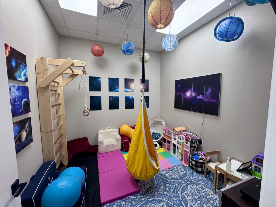 play room with soft padded floor, Swedish ladder to climb, sensory swing, egg chair, peanut balls, play kitchen and toys in a space theme