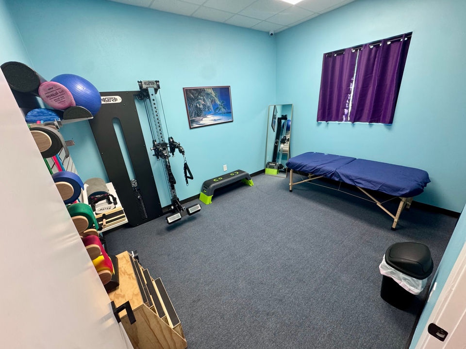 treatment room with exercise cable tower pulley machine, therabands for stretching, and other small exercise equipment as well as a treatment table