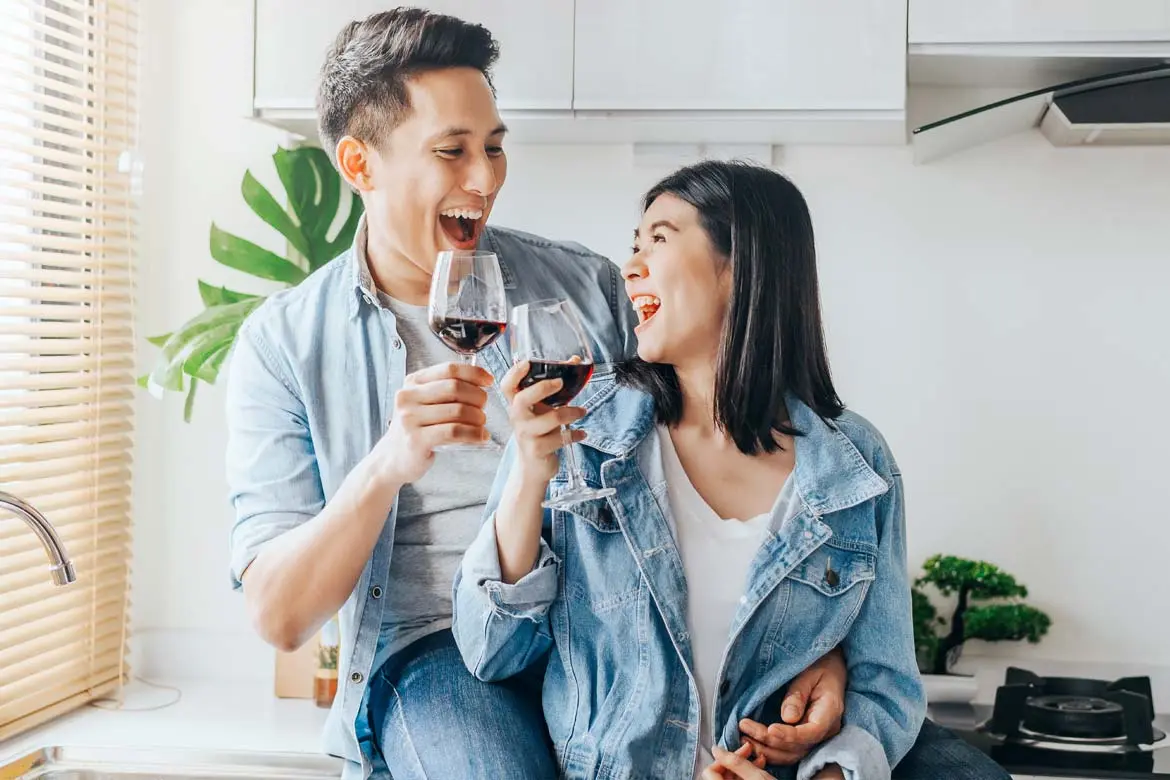 A healthy couple wearing denim jacket and a white t-shirt in the kitchen are drinking a glass of chianti