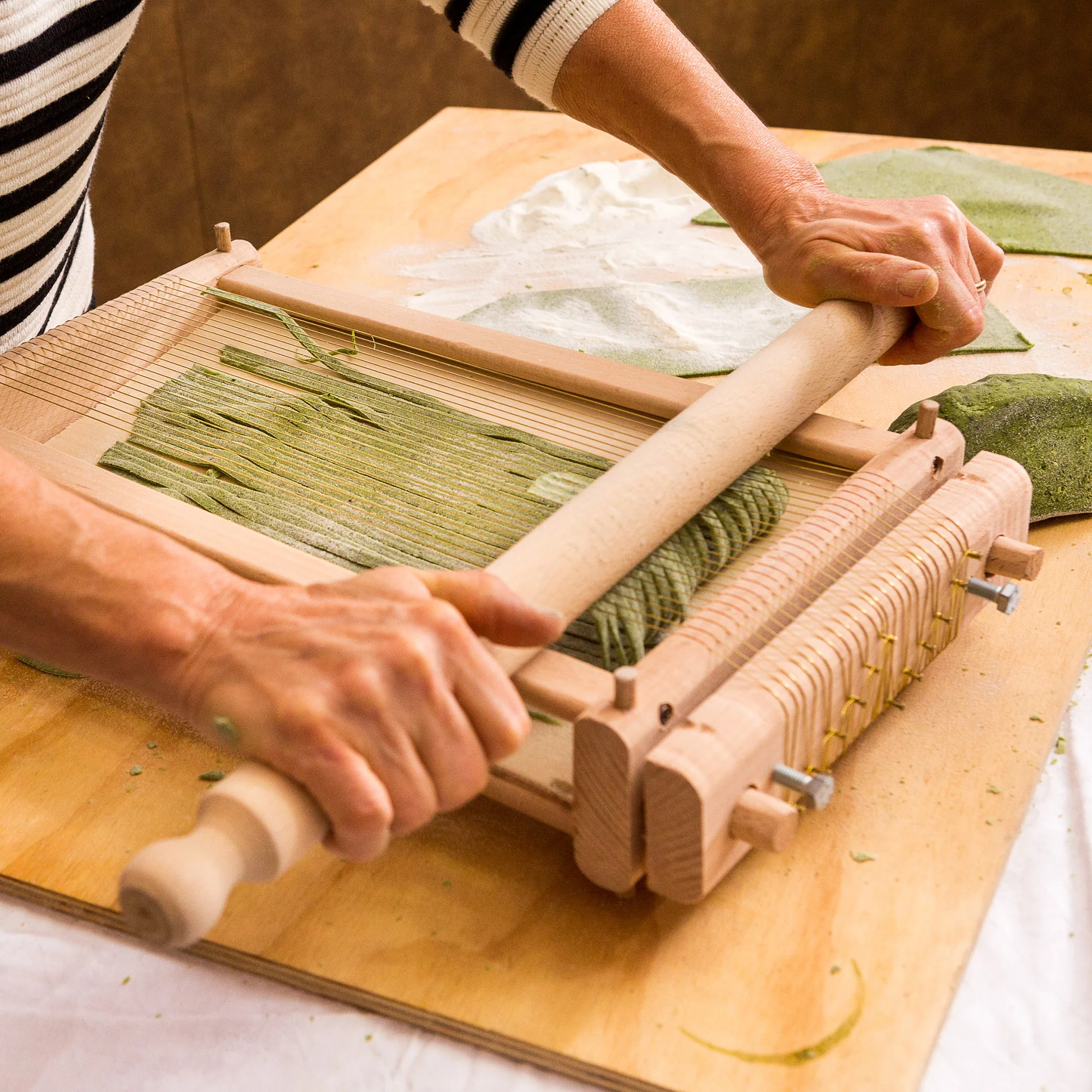 An image of a man rolling pasta on Chittara machine to make Chittara spaghetti